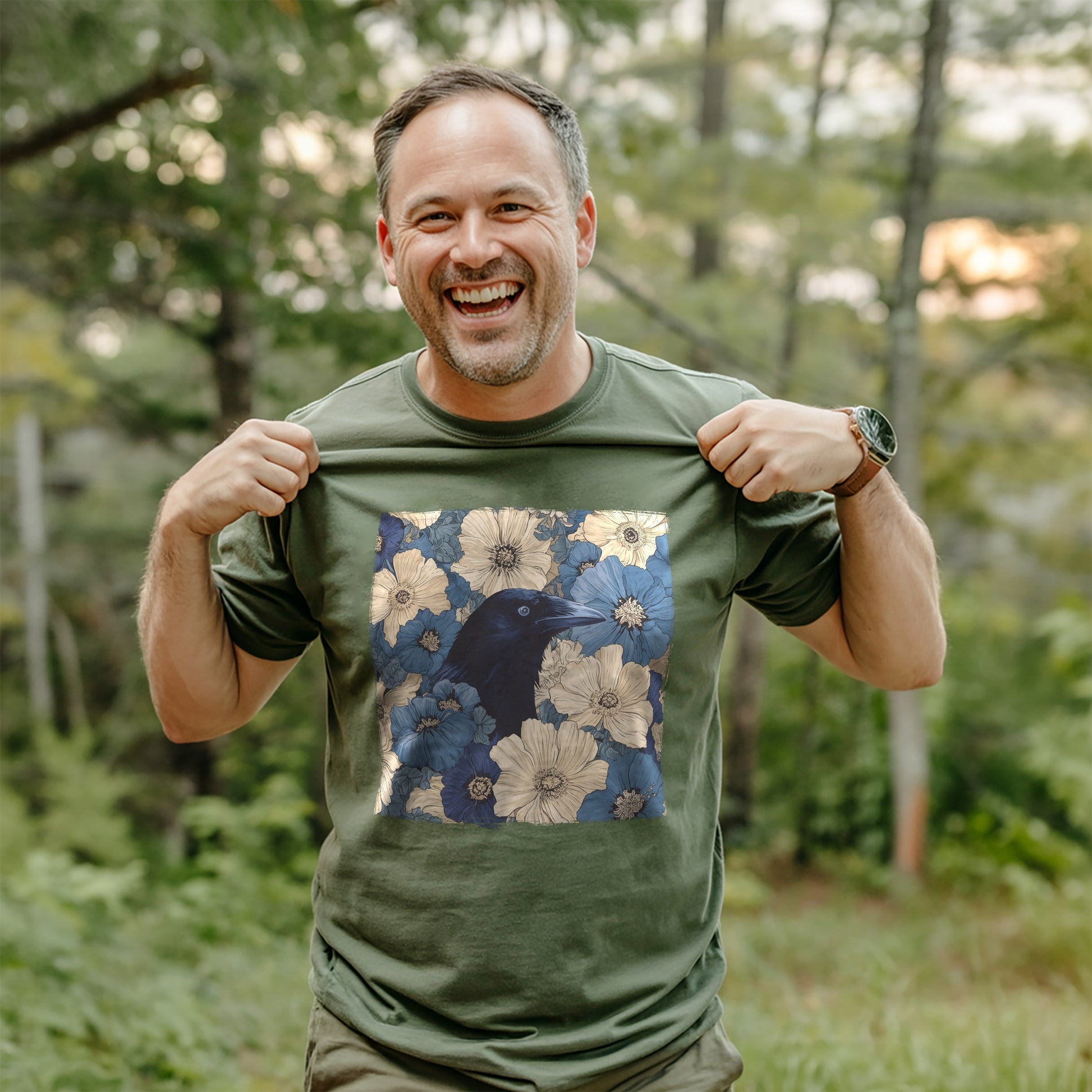Man wearing a military green t-shirt with a raven in flower field design, standing in a forest.