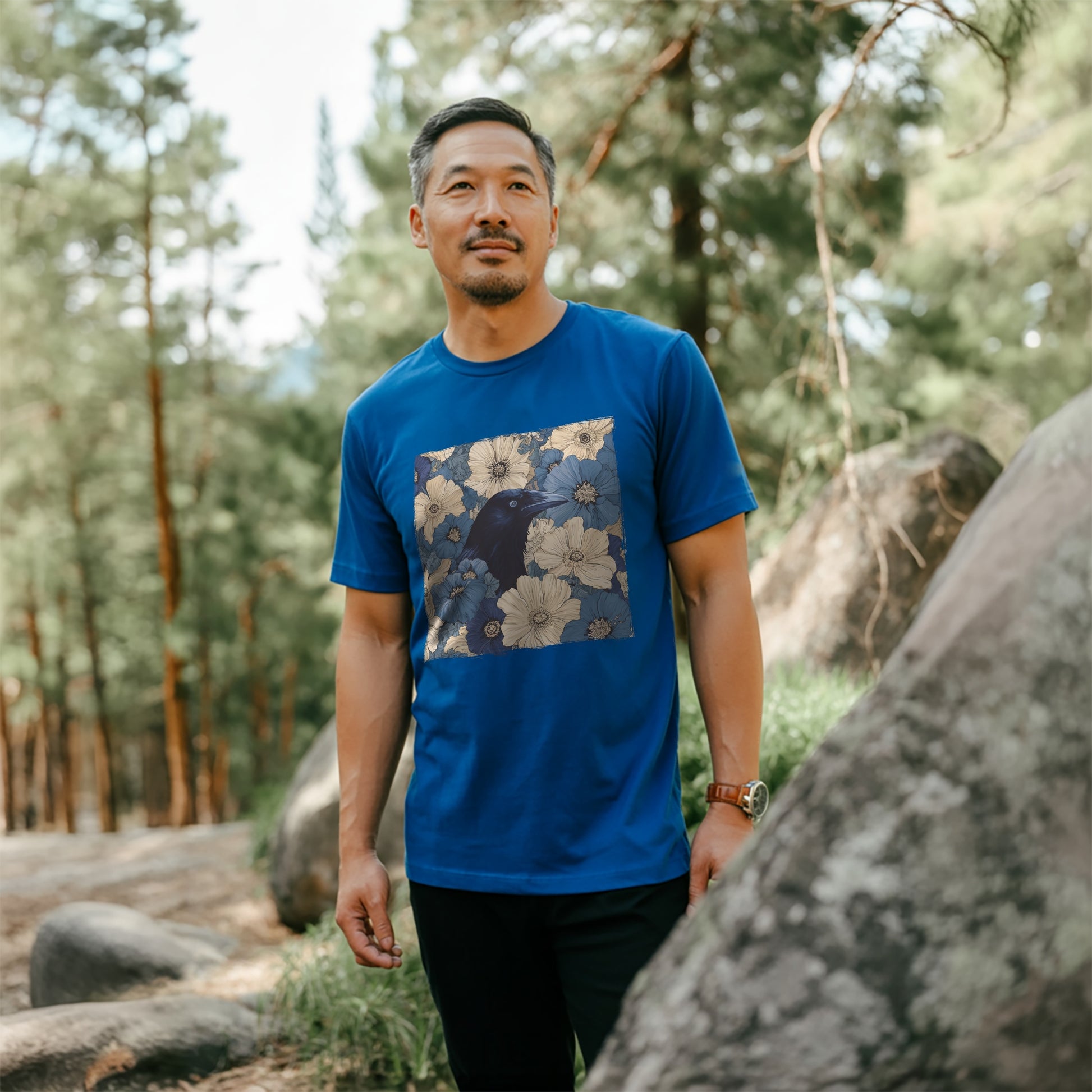 Man wearing a royal blue t-shirt with a raven in flower field in a forest setting