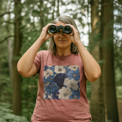 Women in a forest using binoculars, wearing a heather mauve t-shirt with a raven in flower field design.
