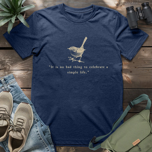heather navy t-shirt featuring a vintage-style beige wren illustration and the quote “It is no bad thing to celebrate a simple life,” laid flat with casual accessories.